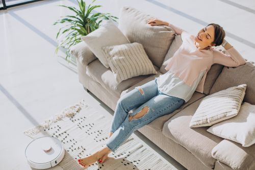 woman relaxing sofa while robot vacuum cleaner doing housework (1)
